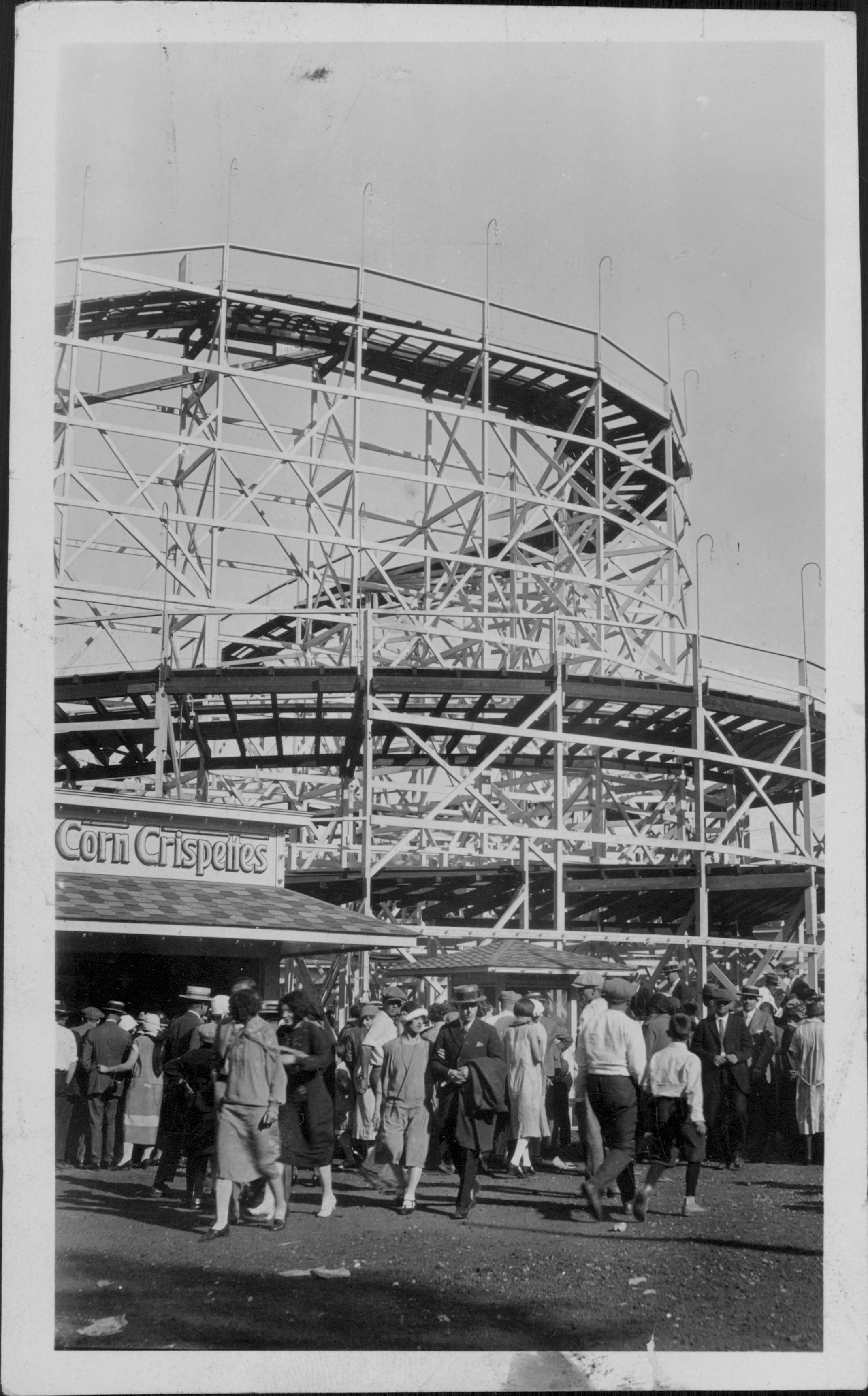 People outside Corn Crisperies with the roller coaster behind at Excelsior Amusement Park