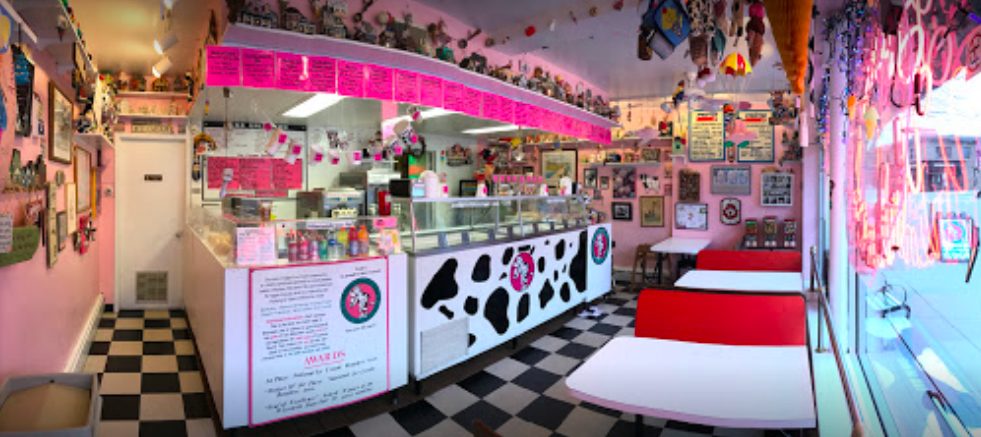 Inside Licks Unlimited in Excelsior, Minnesota — pink walls, a black-and-white checkerboard floor, red vinyl booths, a cow-print ice cream counter and neon signs