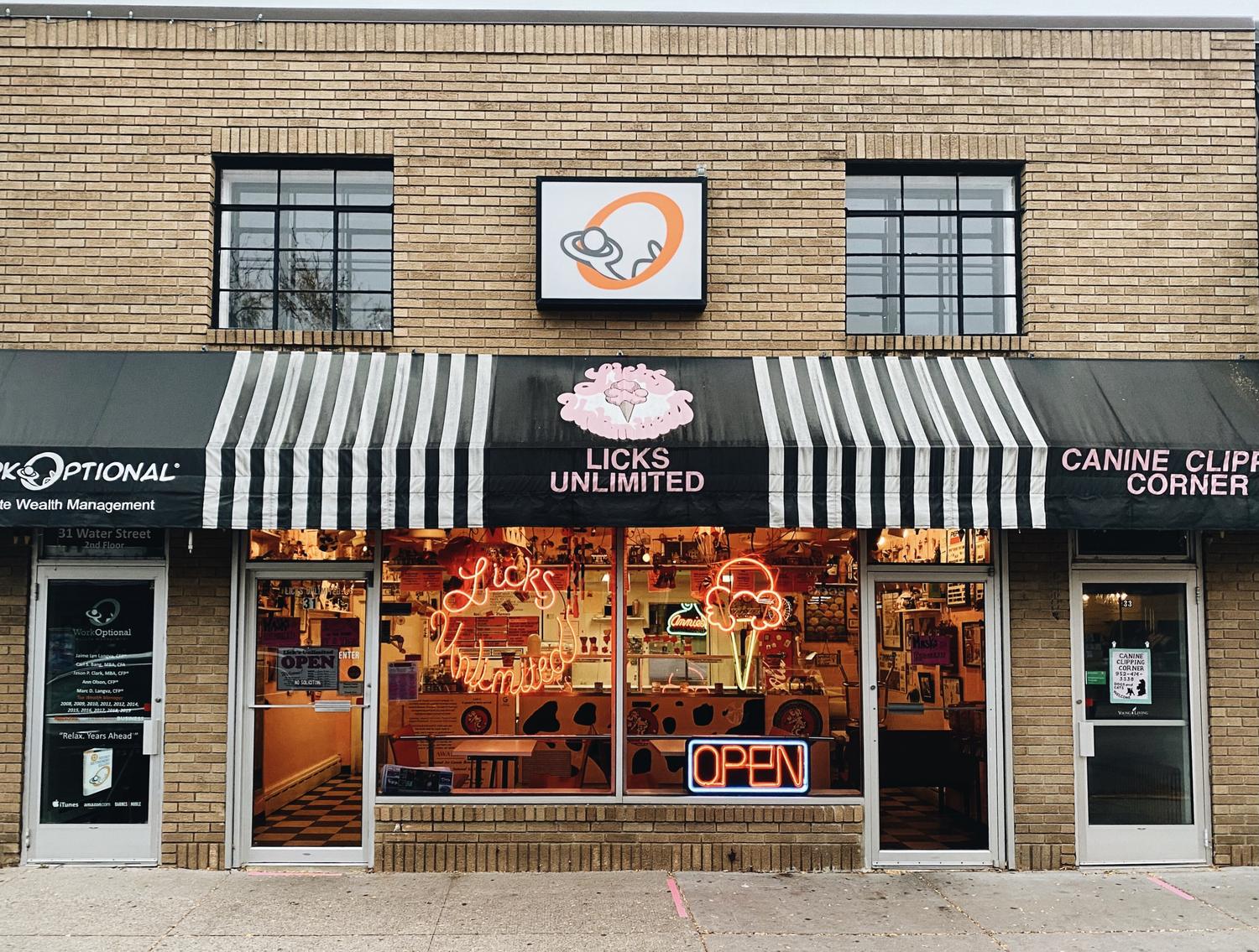 The Licks Unlimited storefront at 31 Water Street in downtown Excelsior, Minnesota — black and white striped awning and a neon Licks Unlimited sign glowing in the window