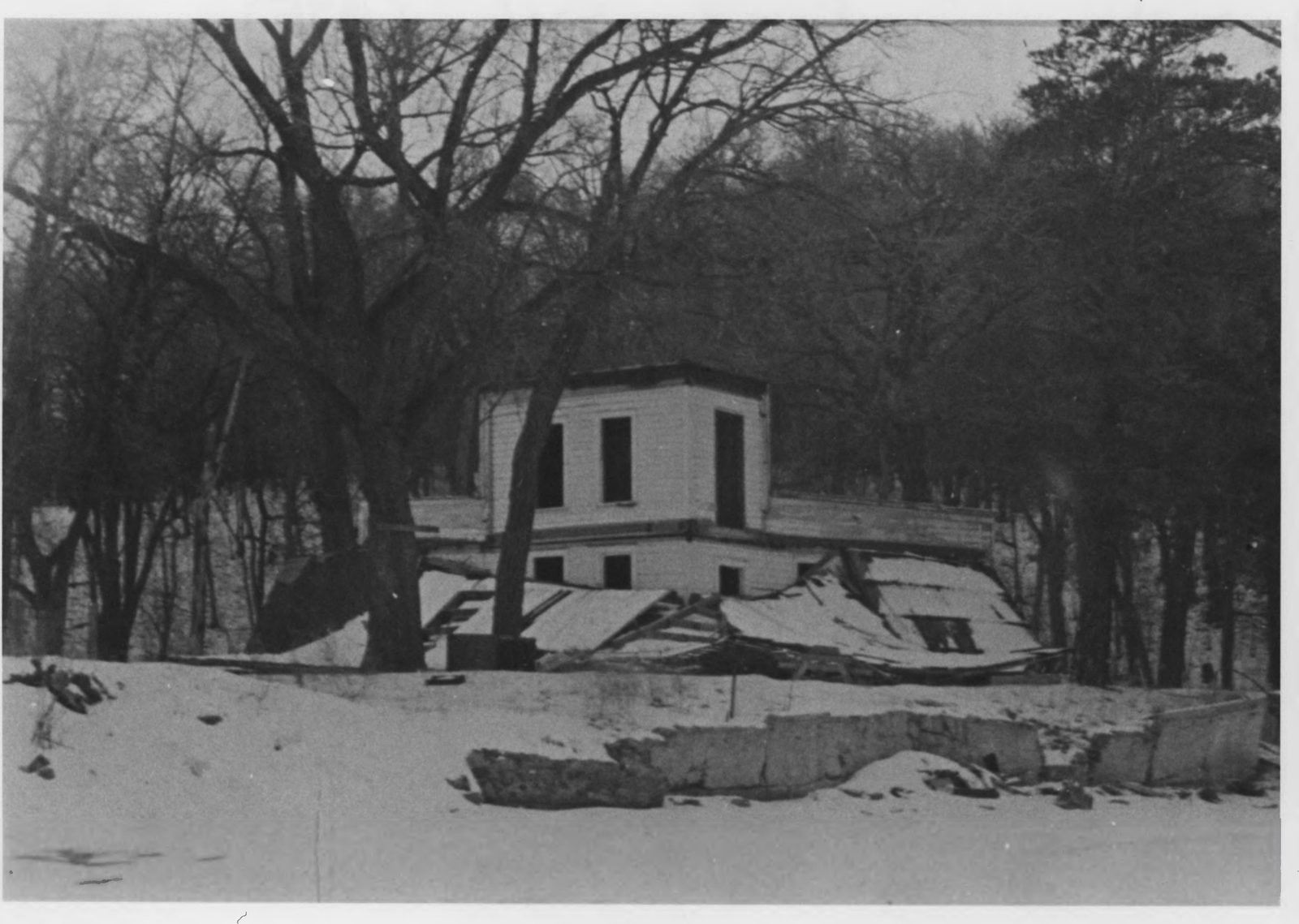 Historic winter photo of Villa Emile on Coney Island, a stripped white two-story shell with a broken seawall in the foreground and snow on the ground