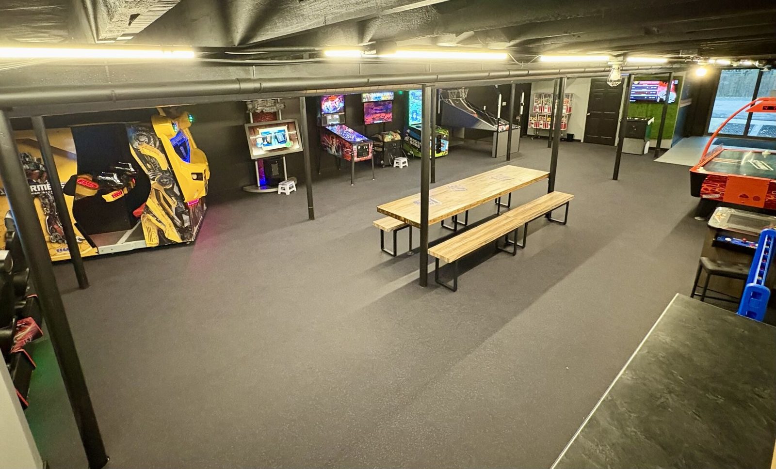The Basement Arcade in Waconia, a carpeted basement room with arcade cabinets, pinball machines, air hockey and a long wooden party table
