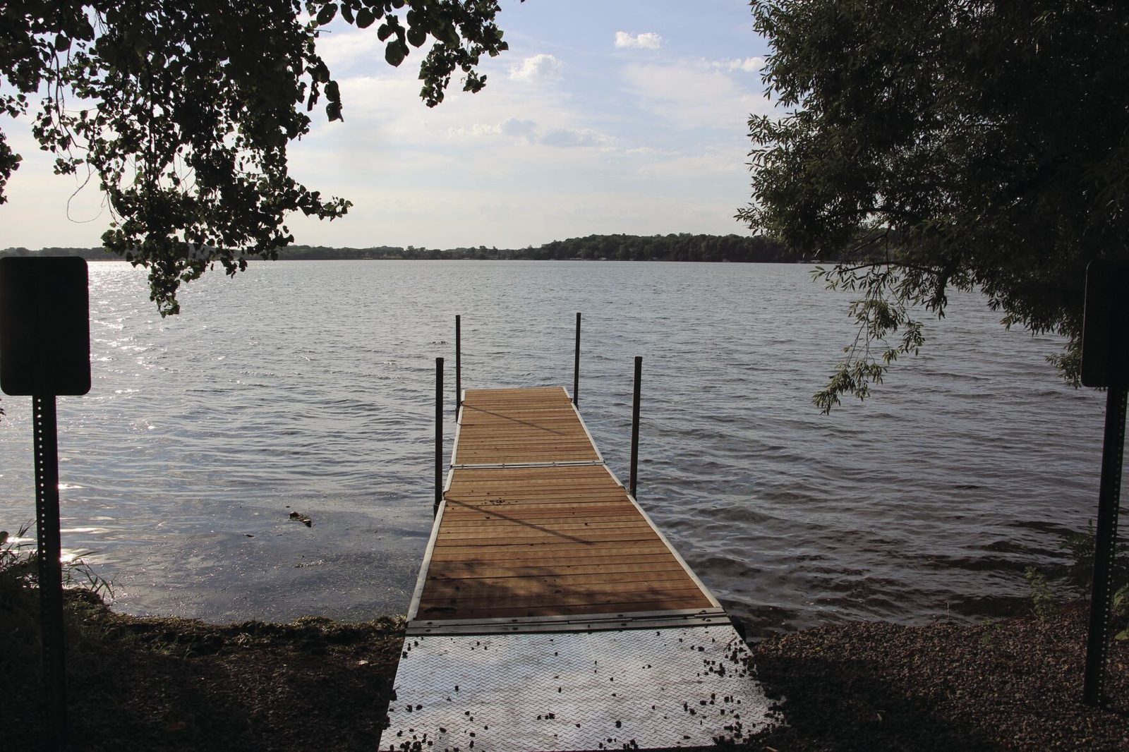 A wooden visitor dock running out from the wooded shore of Coney Island into Lake Waconia