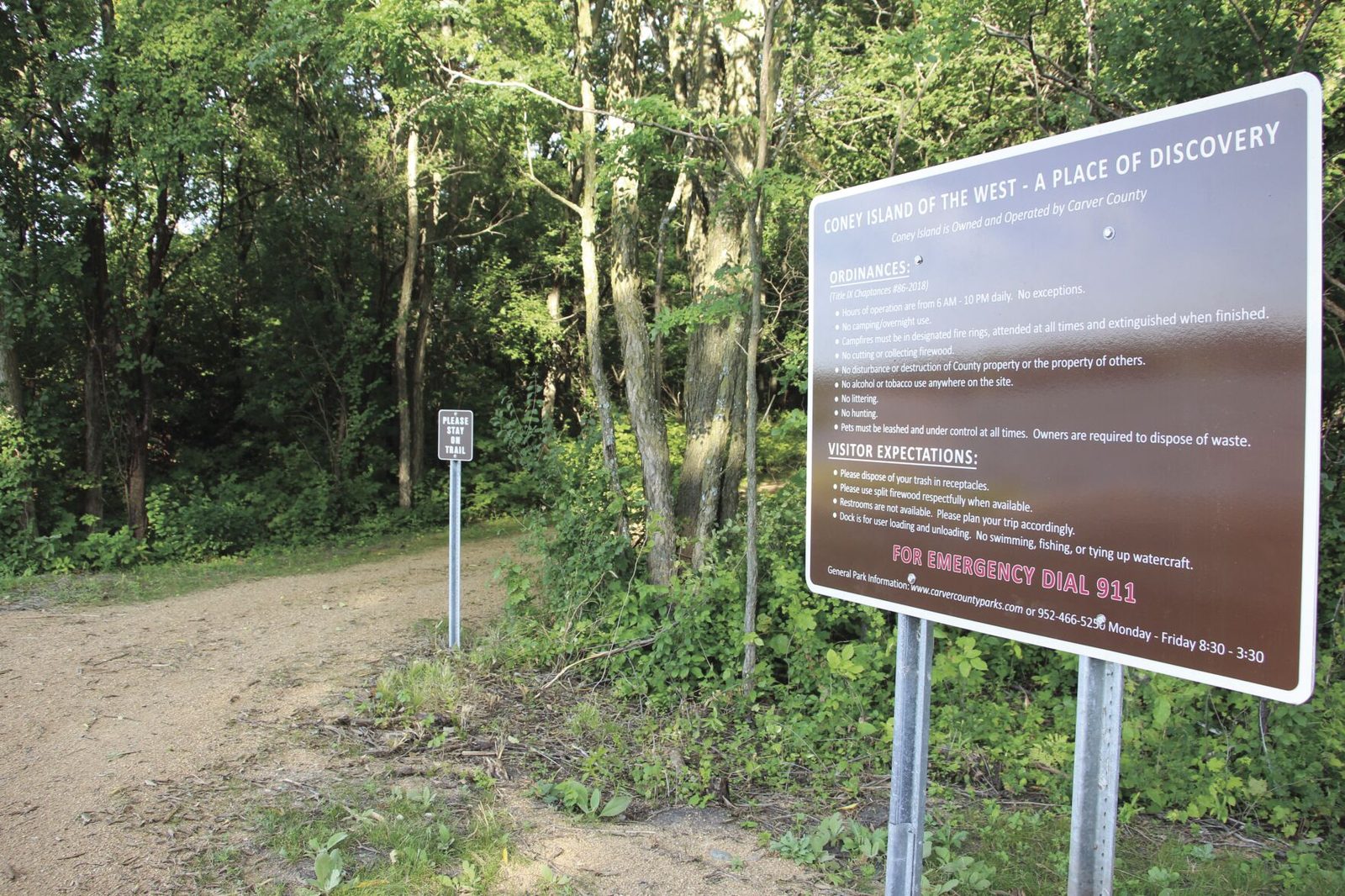A gravel trail through the woods on Coney Island with an interpretive history sign beside it