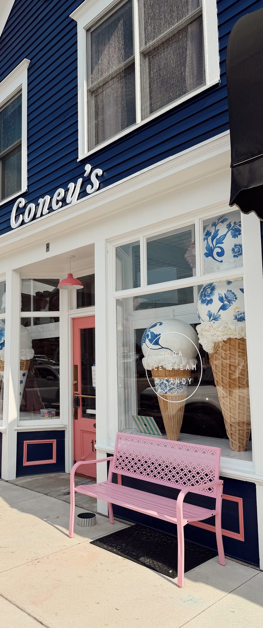 The navy clapboard storefront of Coney's on Main Street in Waconia, with giant ice cream cones in the windows and a pink bench out front