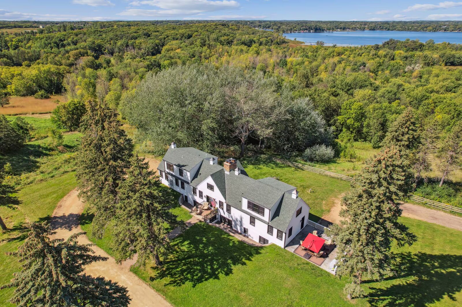 Aerial view of the rolling, partly wooded acreage around the home, showing surrounding trees, open lawn, and Lake Minnewashta in the distance