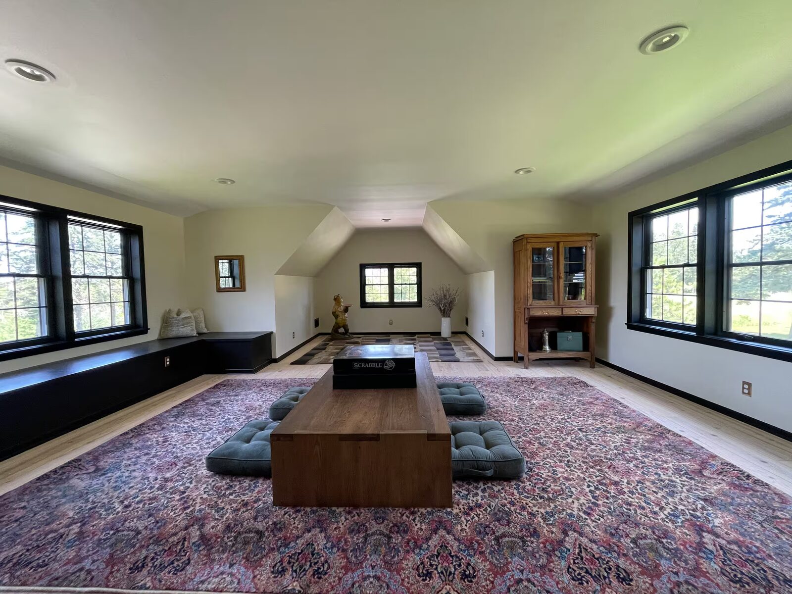 The finished upper great room in the former attic, with a large patterned rug, a low wooden table, and windows on both sides