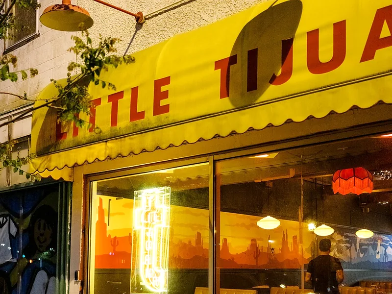 The yellow Little Tijuana awning at dusk with neon in the window